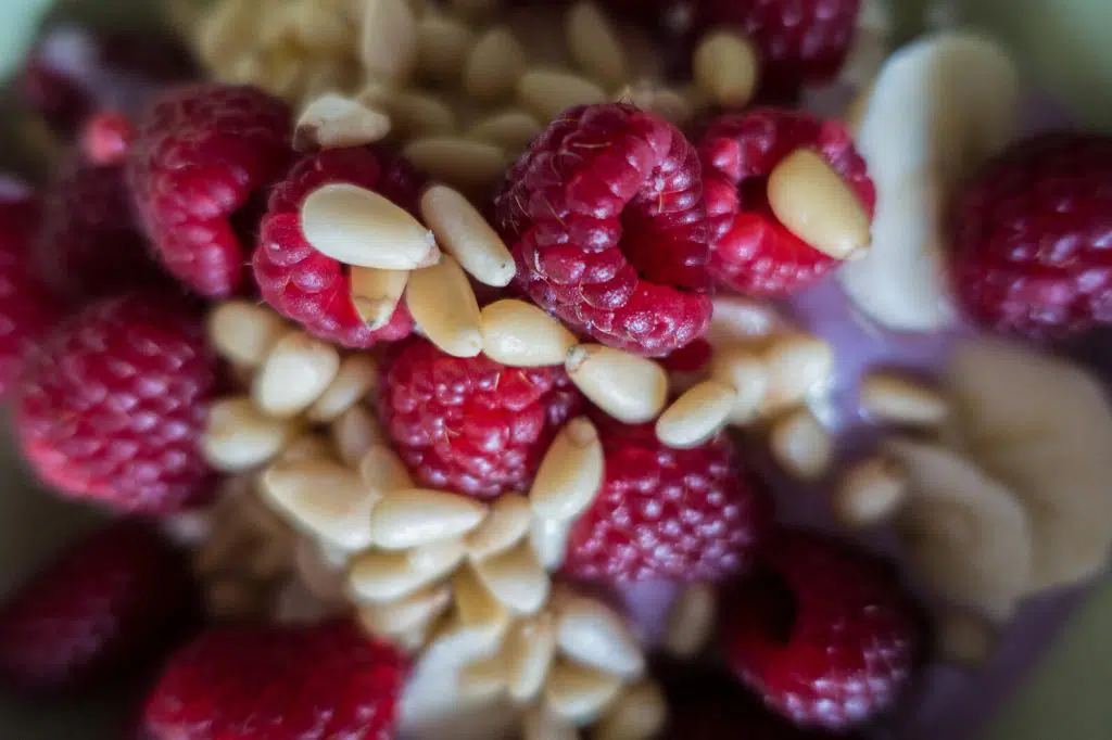 Pine nuts mixed with raspberries on top of a banana smoothie soup mixture.