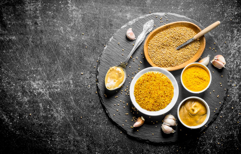 Different types of mustard on a stone Board with garlic.