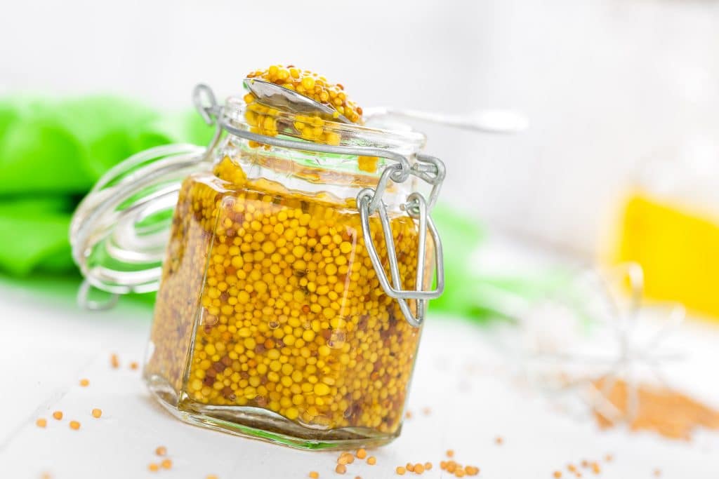 Dijon Mustard in glass jar on white wooden table closeup.