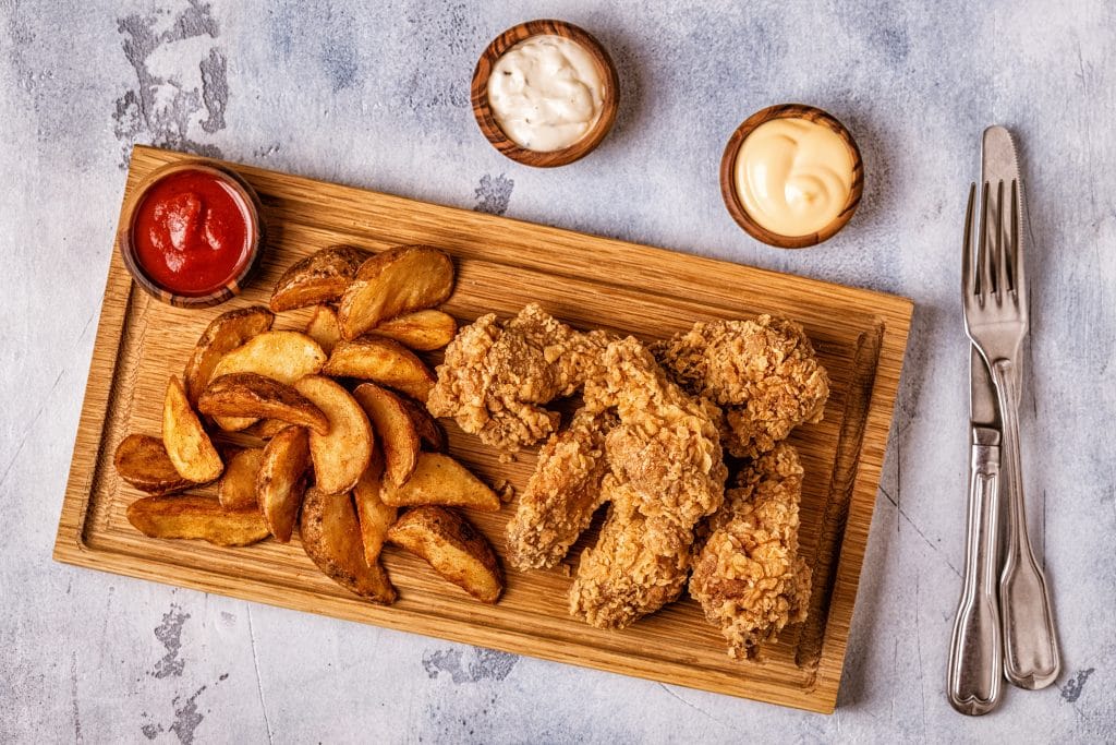 Fried chicken wings with fried potato slices.