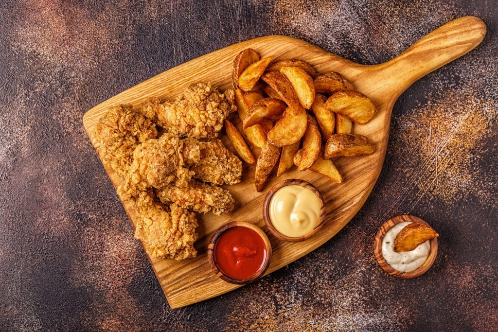 Fried chicken wings with fried potato slices, top view.