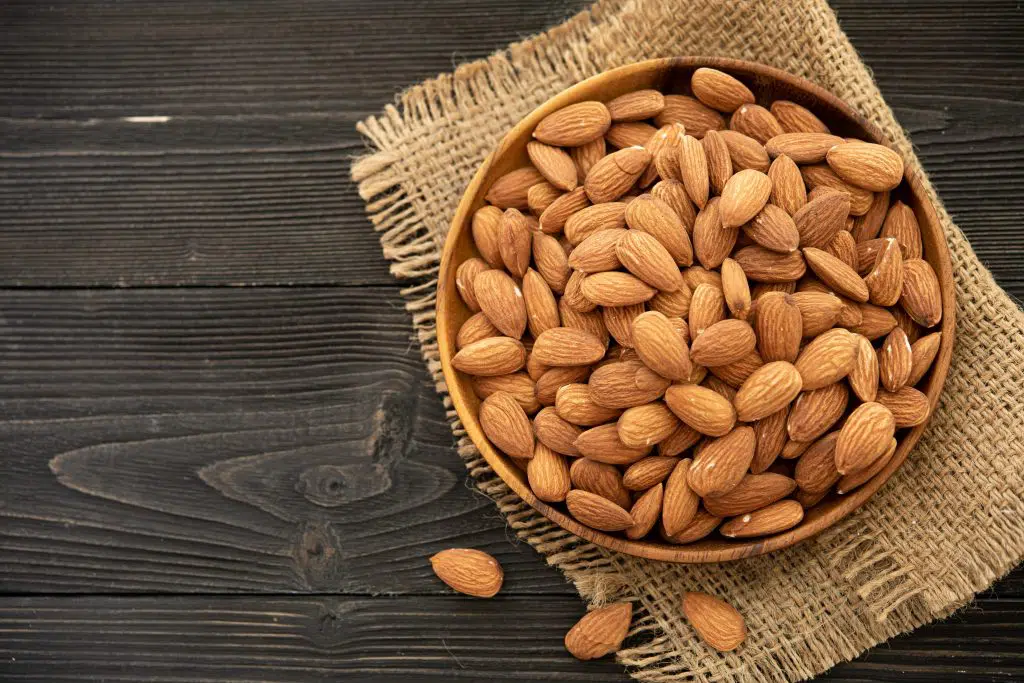 almond in a wooden bowl. on a wooden background, near a bag from