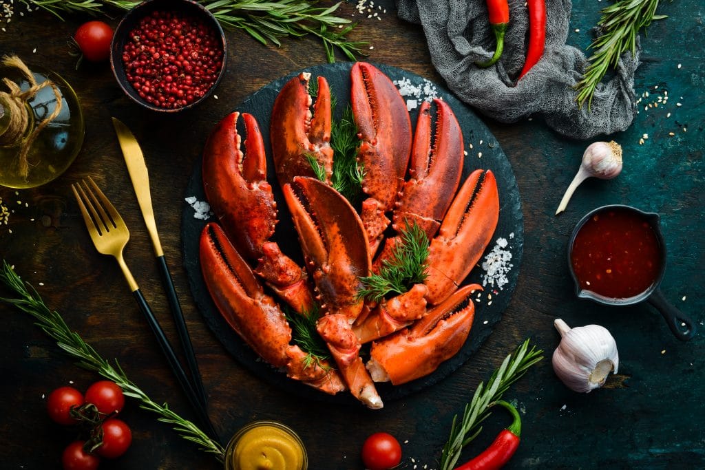 Boiled red lobster claws with spices and parsley on a black stone plate. On a black background. Rustic style. Seafood delicacies.