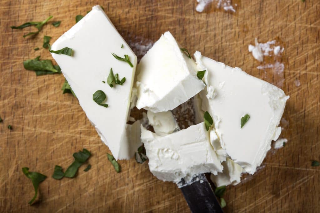 Feta cheese pieces with knife and herbs on wooden background