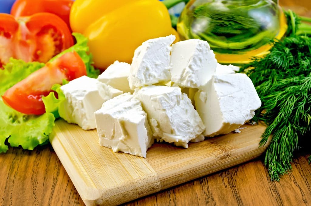 Slices of feta cheese, tomatoes, yellow sweet peppers, lettuce, a bottle of oil, dill on wooden board