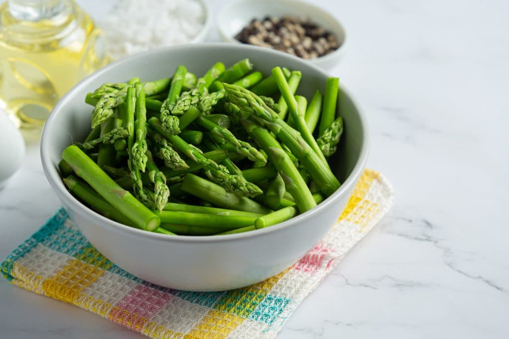 fresh green asparagus in bowl on marble background