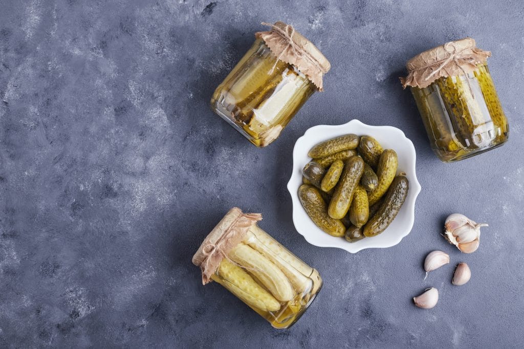 Pickled cucumbers in bowl and glass jars on blue background with garlic. High quality photo