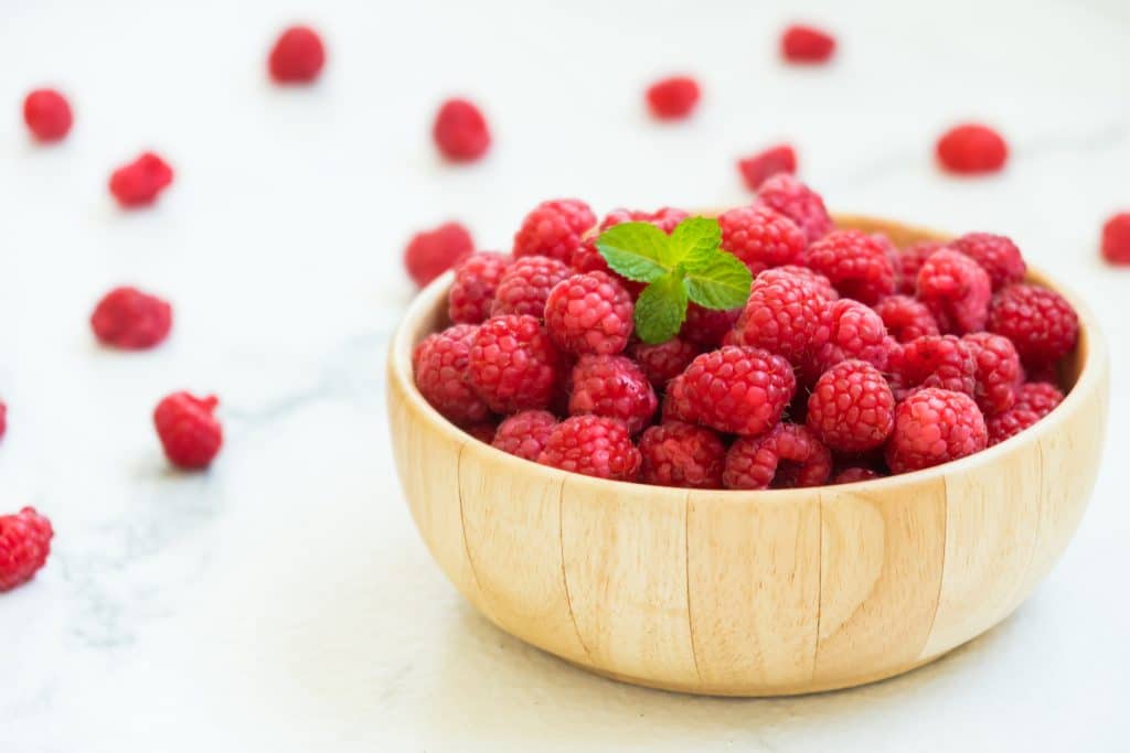 Red raspberries fruit in wood bowl on table