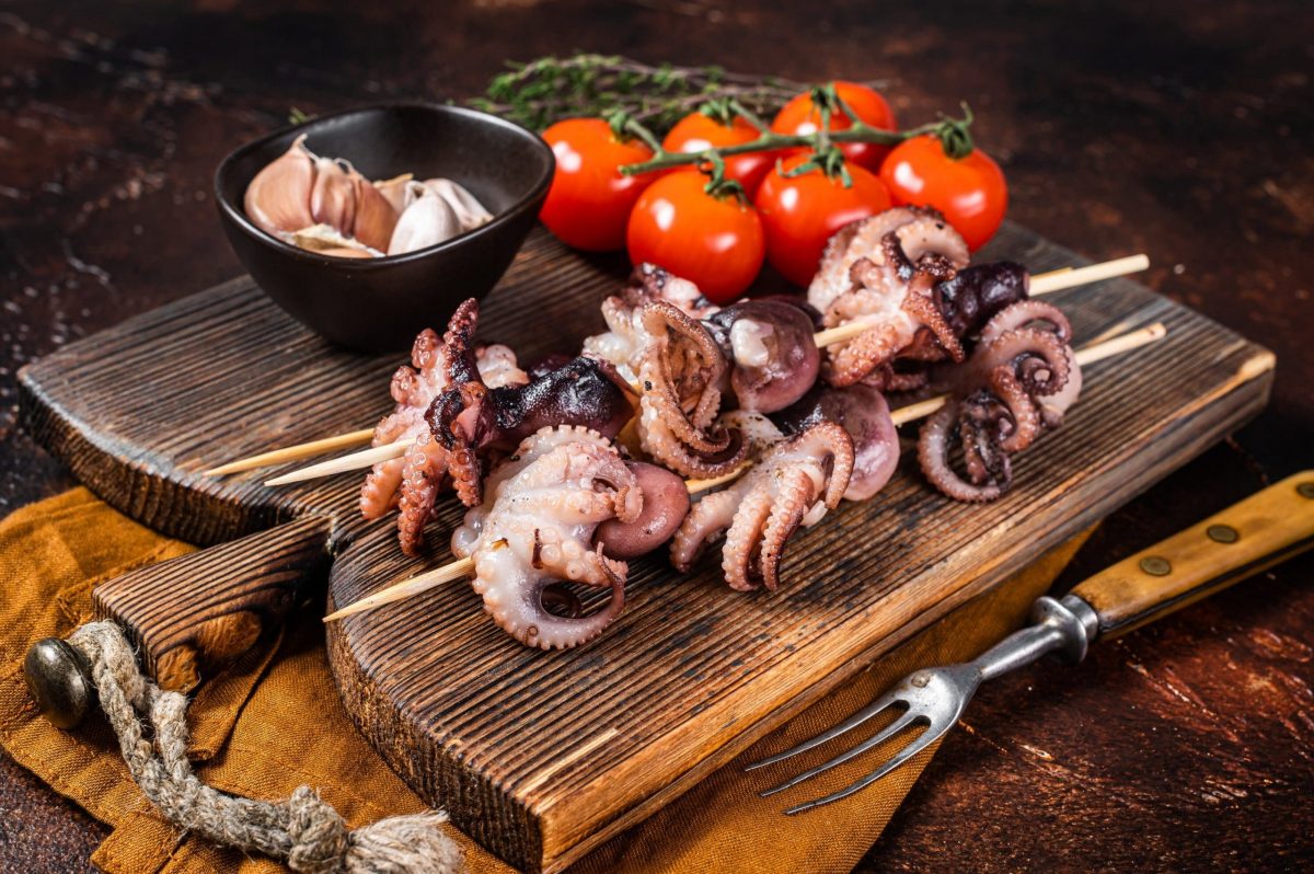 Skewers with bbq roasted baby octopuses. Dark background. Top view.