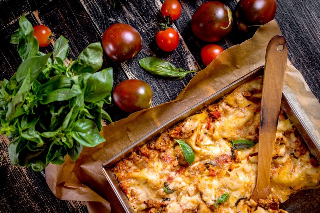 Close-up of a traditional italian lasagna made with minced beef bolognese sauce topped with basil leafs served on a rustic dark wooden table