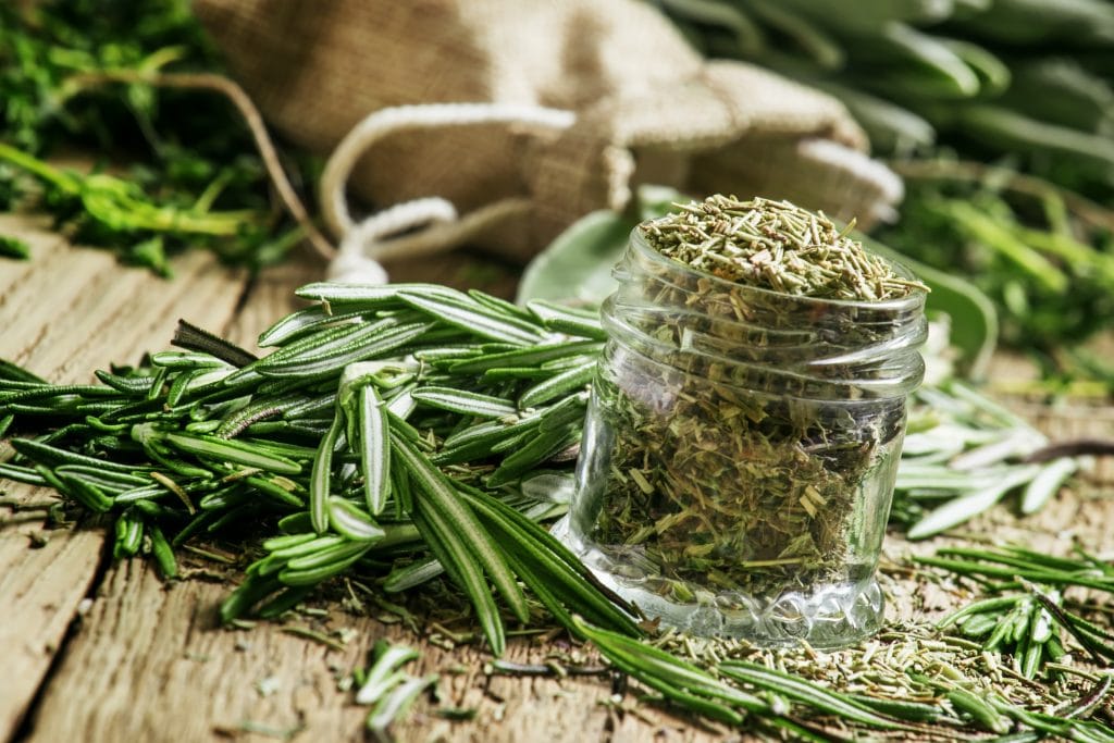 Dried rosemary in a glass jar, branches of fresh rosemary, vintage wooden background, selective focus