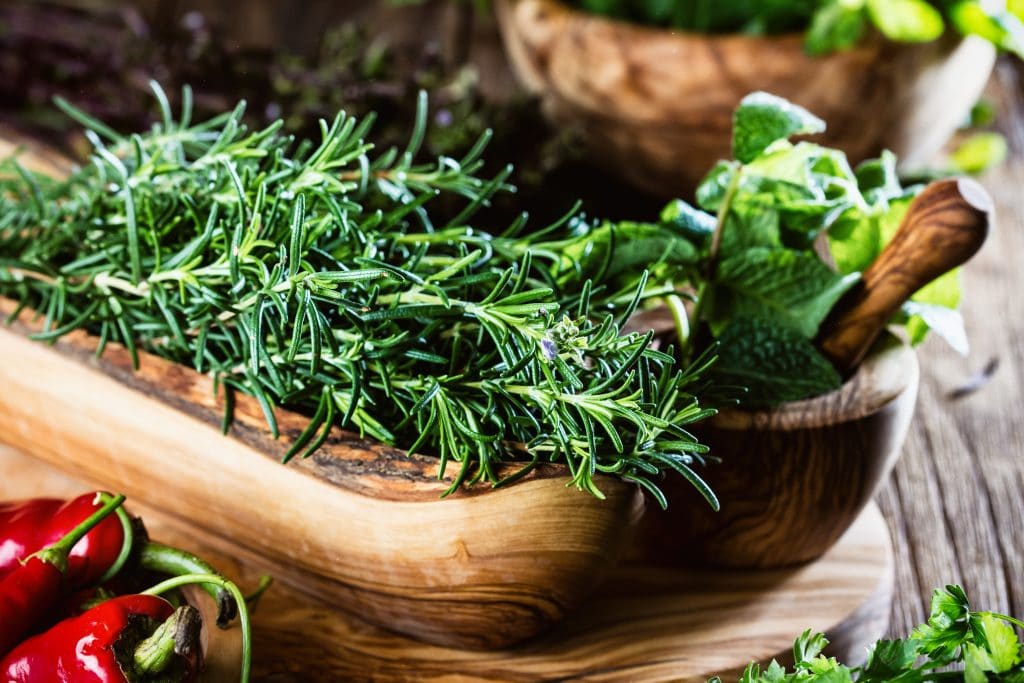 Fresh rosemary in olive wooden bowl on wooden background