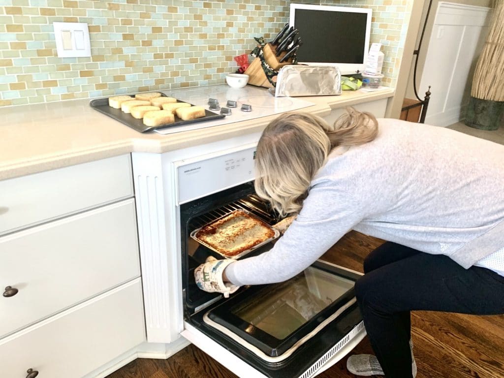 Women in the kitchen taking hot lasagna out of oven for dinner 