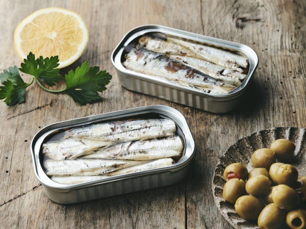open sardines cans and olives on rustic wooden table