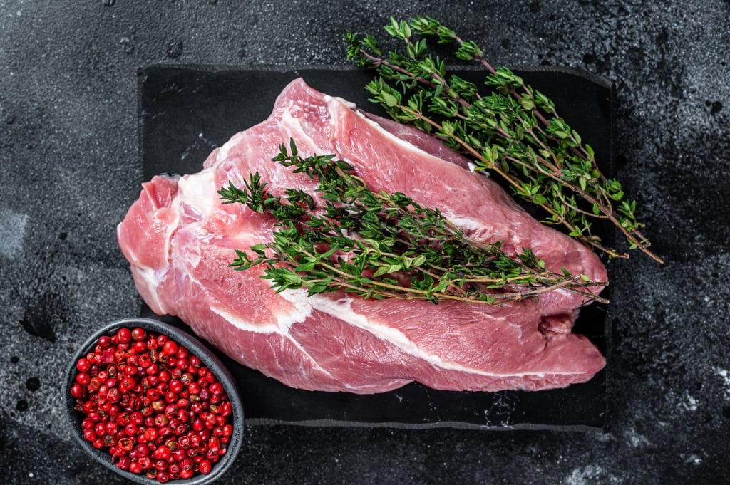 Raw pork shoulder meat cut on a marble board. Black background. Top view.