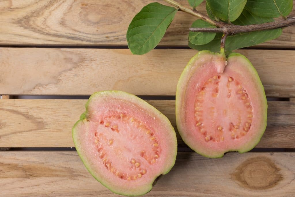 Guava red fruit cut in half fresh on wood background.