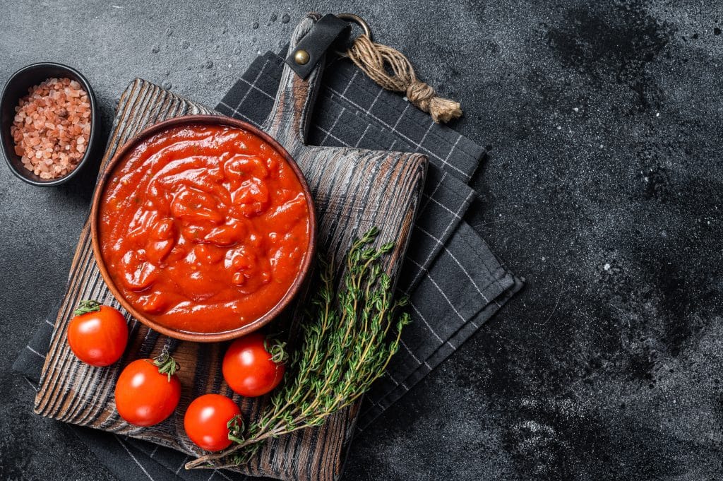 Tomato sauce passata - traditional sauce for italian cuisine. Black background. Top view. Copy space.