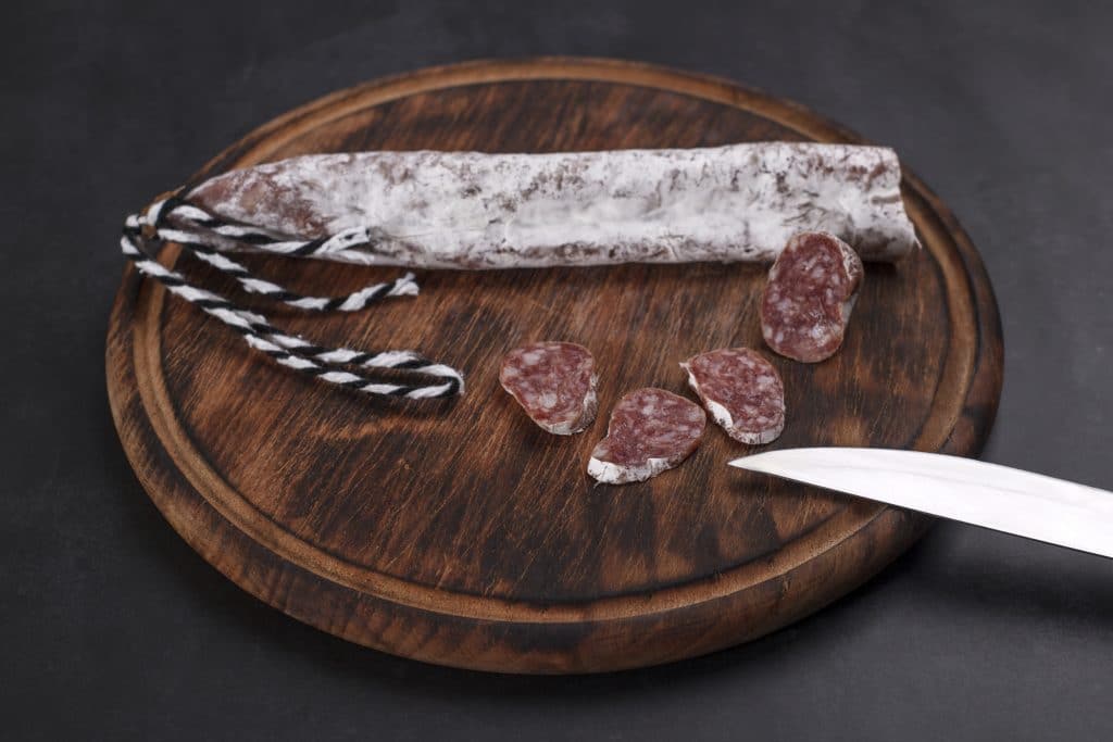 Traditional Catalan thin cured Fuet pork sausage with sliced pieces on a wooden board.