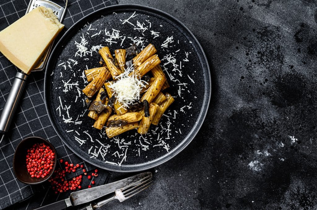 Pasta tortiglioni with black truffle and Boletus edulis, white mushroom. Black background. Top view. Space for text.