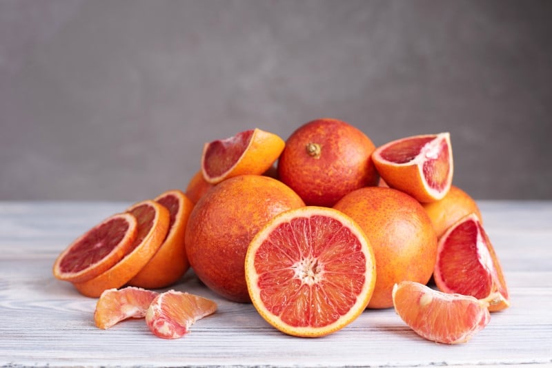 The batch of fresh juicy blood orange on gray wooden background, healthy food, close up.
