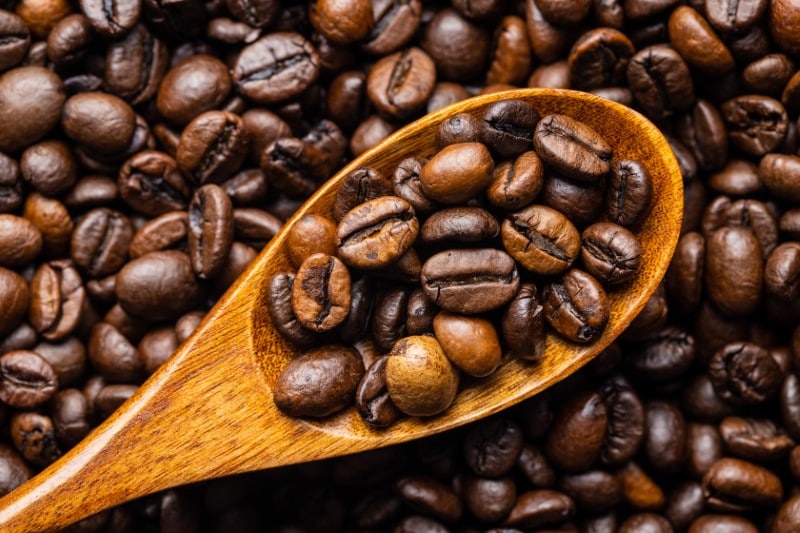 Mixed coffee beans in wooden spoon. Arabica and robusta textured. Top view.