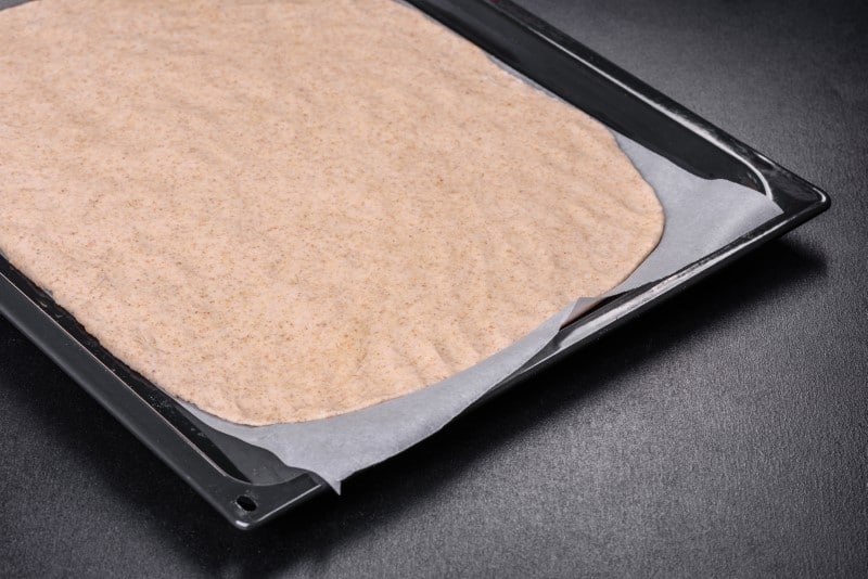 Rolled out prepared raw dough on parchment and baking sheet prepared for cooking pizza